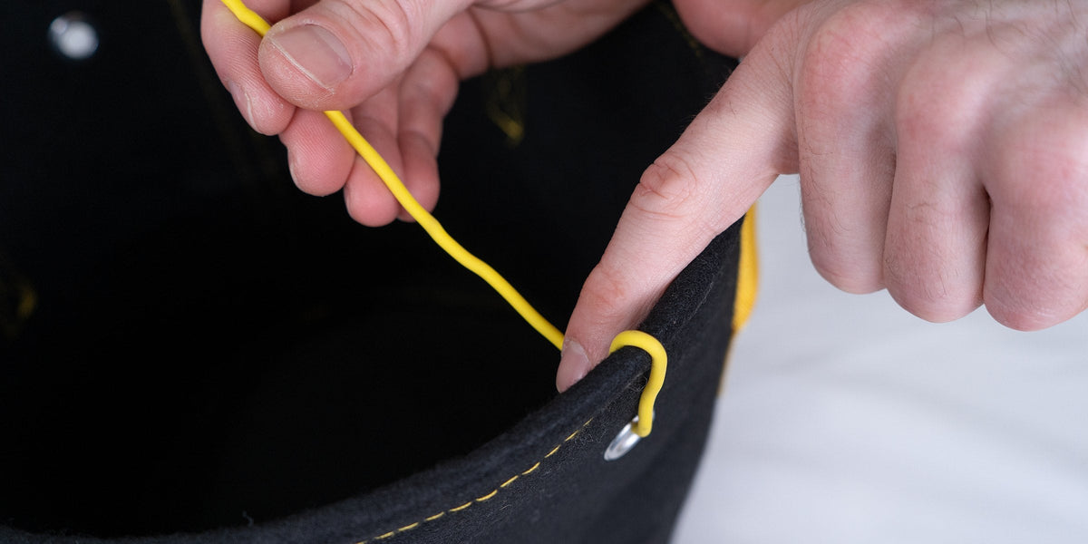 Hands threading yellow soft garden wire through a metal grommet on the rim of a black fabric grow bag