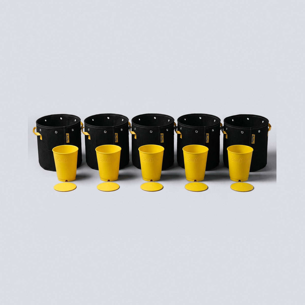 Seed to Pot Set: five yellow seed starting cups with bottom plates in front of five 1 gallon black fabric grow bags